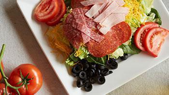 Antipasto Salad · A blend of romaine and spinach topped with tomatoes, red onions, black olives, chopped ham a...