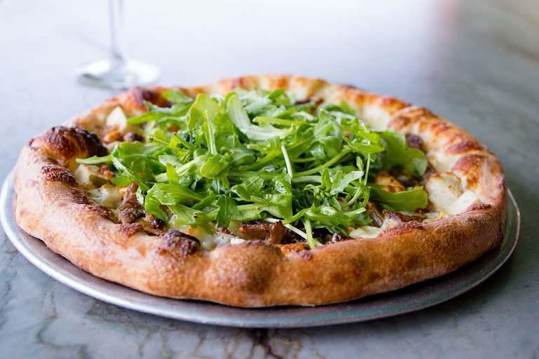 Pear-Gorgonzola-Arugula Pizza · Candied walnuts, caramelized onions, dates, sliced pears, blue cheese crumbles, mozzarella, drizzled with garlic basil oil then baked - topped with fresh arugula.