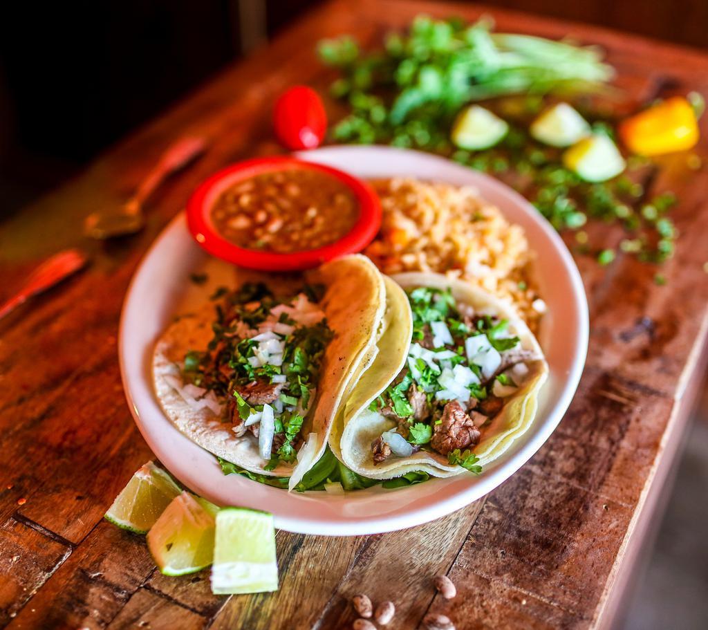 Grilled Steak Tacos · Three traditional soft corn tortillas filled with tender chargrilled steak, cilantro and onions, rice and beans.