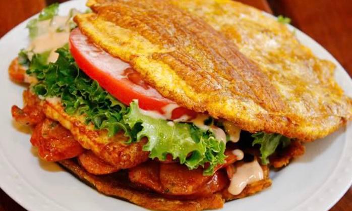Pernil Patacones · Roasted pork Fried Green Plantain sandwich with Grilled Cheese topped with lettuce, tomato, our signature Pink mayo, and ketchup.