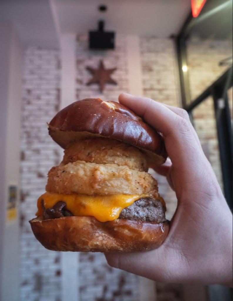 The Fifty Burger · Double Smash Burger topped with bacon, cheddar, smokey BBQ, and 2 onion rings on a pretzel bun.