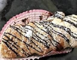French Horn · Flaky puff pastry filled with vanilla custard.  Top is drizzled with chocolate and dusted wi...