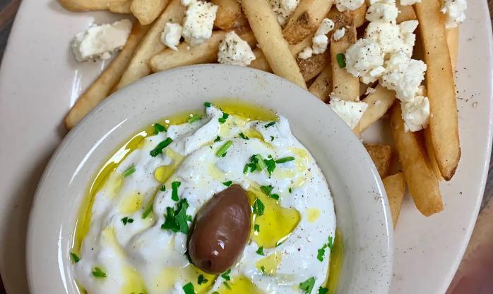 Feta Fries with Tzatziki · Tsatsiki lightly drizzled with Greek olive oil and Kalamata olive, alongside fries topped with feta and Greek spices.