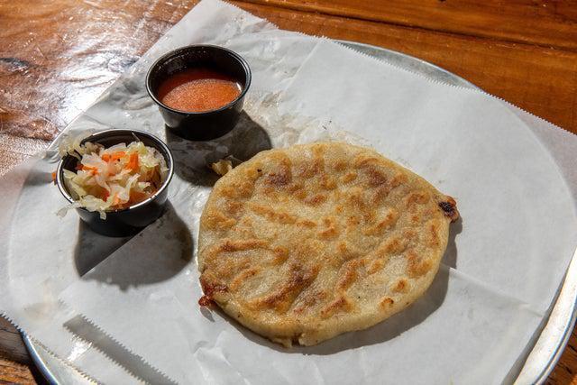 Pupusa Revueltas · Origin: San Salvador, El Salvador. Handmade thick corn tortillas stuffed with ground pork, cheese, and refried beans. Topped with curtido slaw and warm tomato sauce.