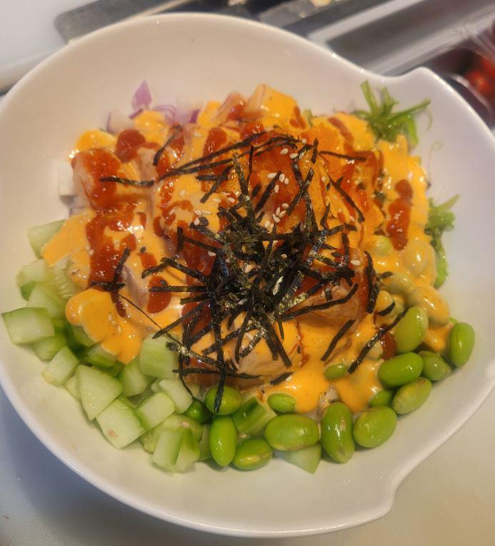 Passion Salmon Poke Bowl · Spicy salmon, cucumber, red onion, edamame, masago, seaweed salad, white rice, topped with sriracha sauce.
