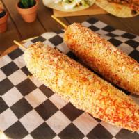 Elotes Street Corn Stick · Buttery whole corn on a stick, smothered in yum yum sauce, topped with Cotija cheese, and sp...