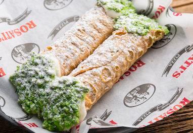 Cannolis · Crisp Sicilian pastry shells filled with sweetened ricotta and chocolate chips, dipped into pistachios and covered with powdered sugar.