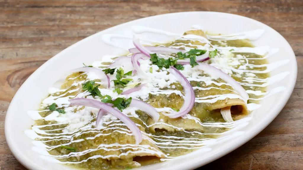 Enchiladas Verdes · Handmade corn tortillas dipped in a tomatillo and green chile sauce filled with roast chicken and garnished with queso fresco, crema, onions, and cilantro. Served with rice and beans.
