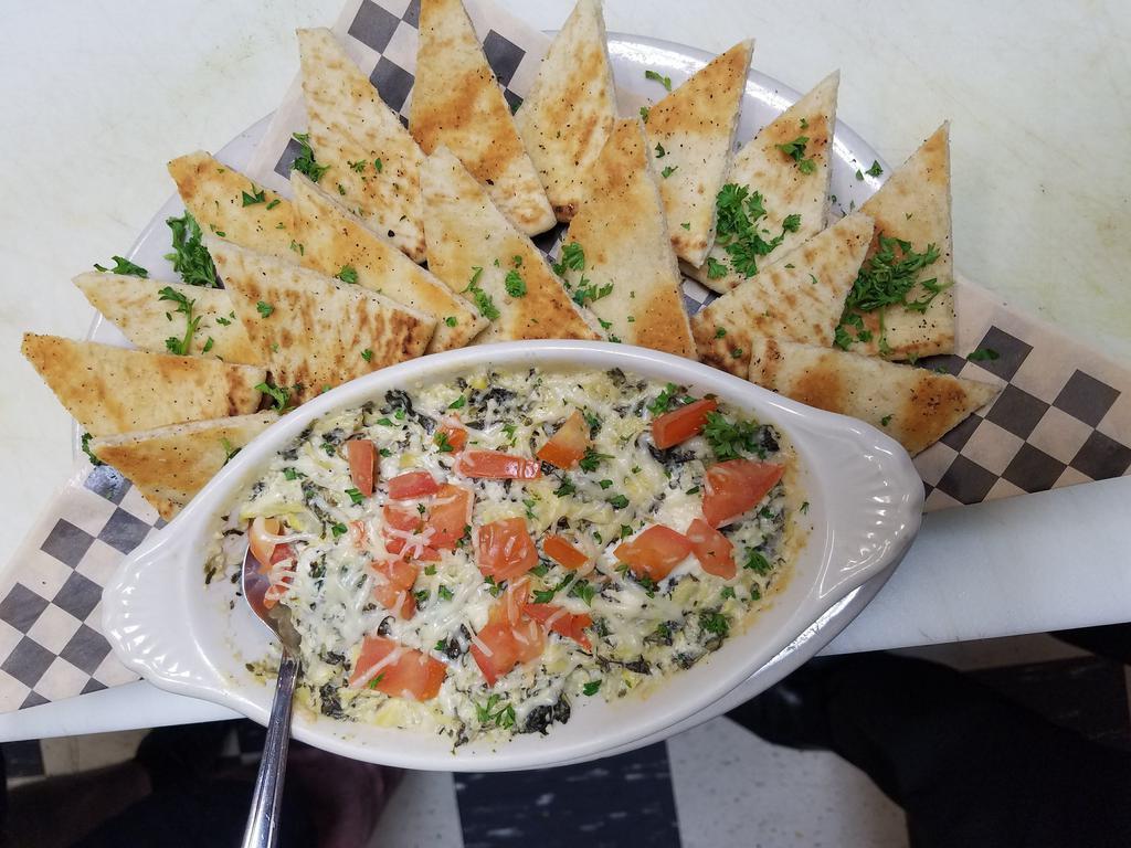 Spinach Artichoke Dip · Creamy artichoke and spinach dip made in-house. Baked with tomato and Parmesan cheese and served with toasted pita bread seasoned with garlic and pepper.