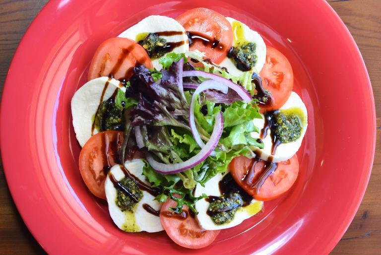 Caprese Salad · Fresh mozzarella, tomatoes, spring mix, thin sliced red onions, homemade pistachio pesto and balsamic dressing.