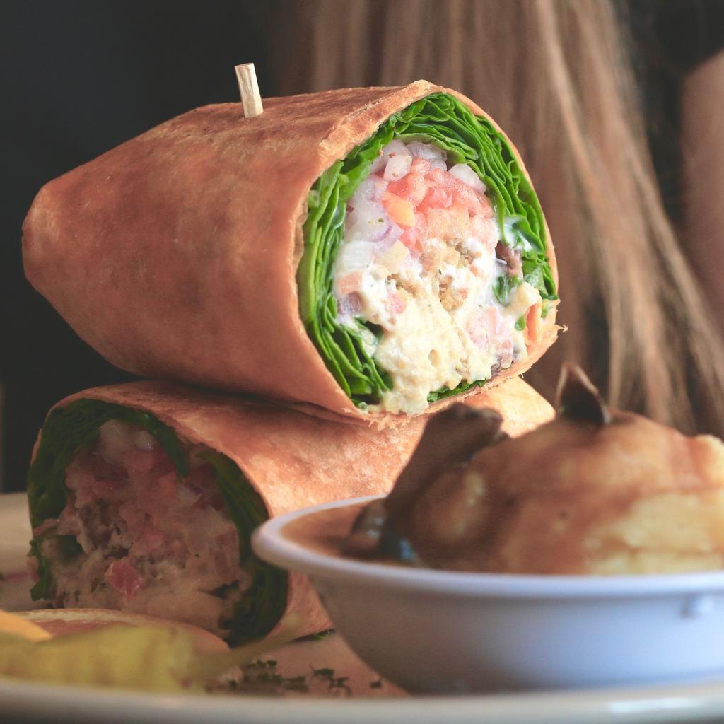 Falafel Wrap · A wheat tortilla stuffed with chickpea falafel patties, tomatoes, vegan tzatziki sauce, purple onions, spinach, hummus and olives.