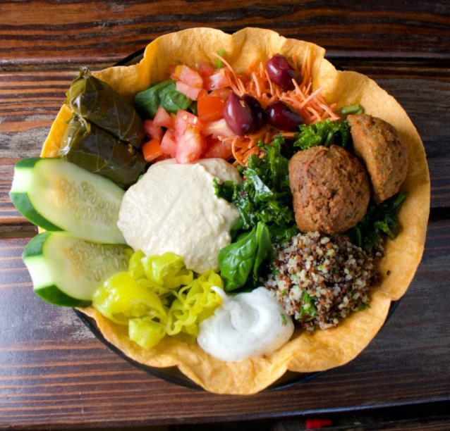 Med Bowl · Whole wheat tortilla-lined bowl filled with quinoa tabouli, kale salad, vegan tzatziki, green olives, falafel patties, cucumbers, tomatoes, carrots, dolmas, and hummus.