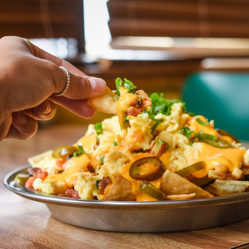 Breakfast Nachos · Enough for 4. House-made tortilla chips topped with scrambled eggs, avocado corn salsa, nacho cheese sauce, chopped bacon, jalapenos, sour cream and scallions.