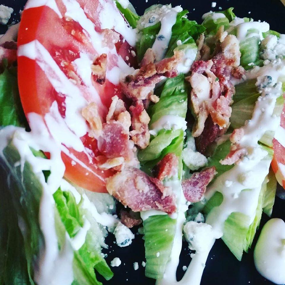 Wedge Salad · Iceberg wedges topped with bacon, blue cheese crumbles, and beefsteak tomatoes finished with blue cheese dressing.