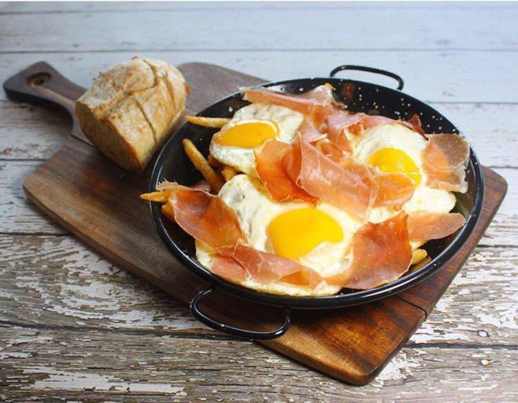 Huevos Estrellados · A very typical spanish dish with french fries topped with three fried eggs and serrano ham or chistorra.