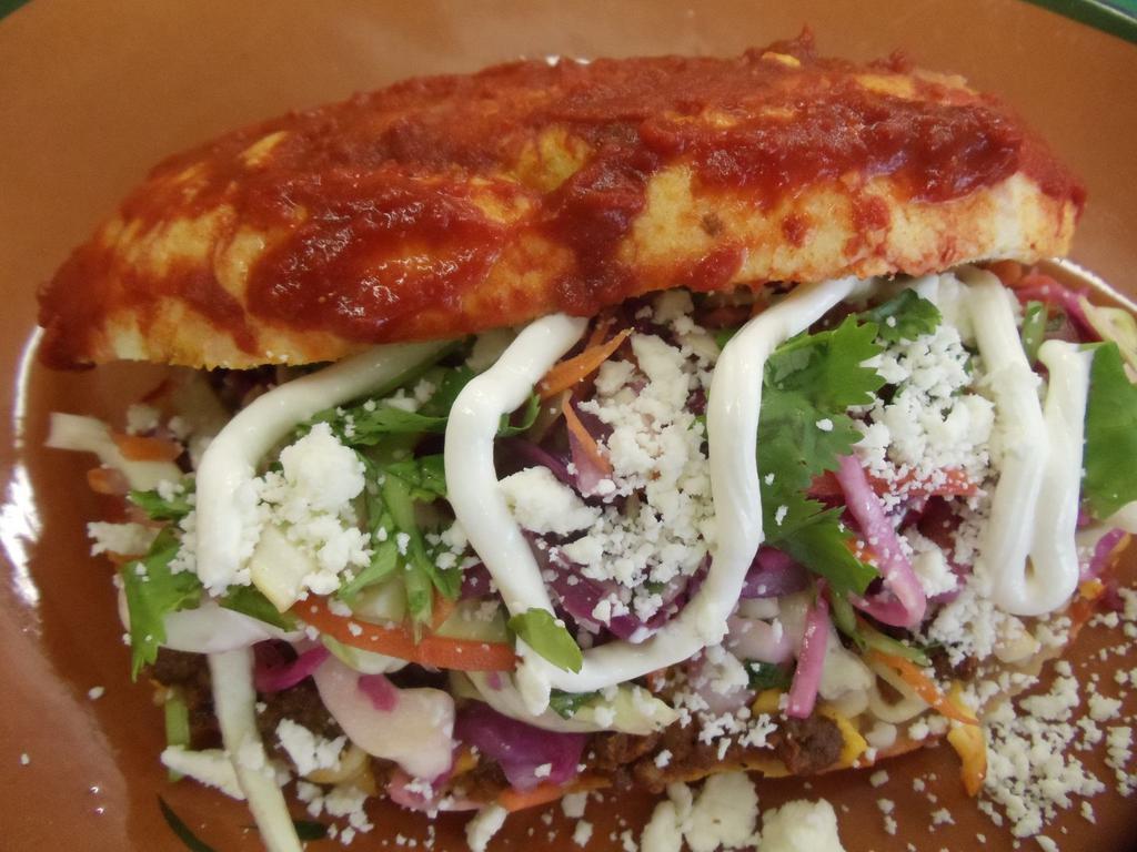 Shredded Beef Pambazo · Mexican sandwich drenched in a delicious guajillo sauce filled with cheese, refried beans, Mexican style coleslaw, queso Fresco, & sour cream.