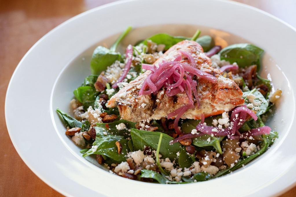Wild Salmon Spinach Salad* · Grilled and sustainable Coho salmon on top of spinach salad mixed with grilled pears, candied hazelnuts, goat cheese, pickled red onions and tossed with warm Champagne bacon vinaigrette.