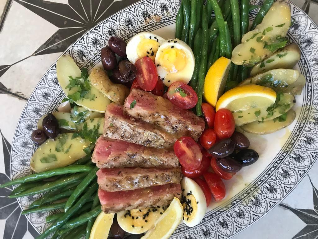 Tuna Nicoise · Classic salad from Nice, France. Fresh yellowfin tuna seared rare. The tuna is served atop a salad Arugula, haricots verts, lhard boiled eggs, and niçoise olives. Anchovy vinaigrette.