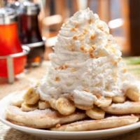 Fresh Banana Whipped Cream Pancakes · Five fluffy buttermilk pancakes with bananas inside and topped with whip cream and macadamia...