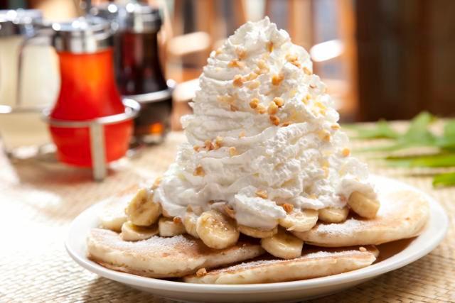 Fresh Banana Whipped Cream Pancakes · Five fluffy buttermilk pancakes with bananas inside and topped with whip cream and macadamia nuts.