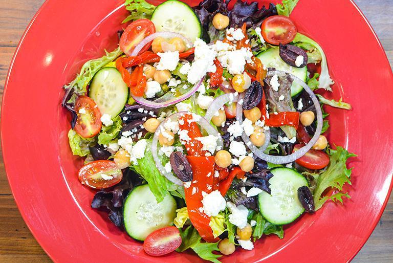 Greek Salad · Fresh crispy romaine and spring mix lettuce topped with cherry tomatoes, cucumbers, chickpeas, red roasted peppers, Kalamata olives, feta cheese and thin sliced red onions dressed with homemade balsamic vinaigrette dressing. Add protein for an additional charge.
