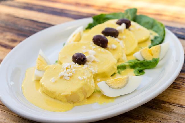 Papa a la Huancaina · Slices of boiled potatoes topped with Aji Amarillo chili and cheese sauce, garnished with Queso Fresco and olives.