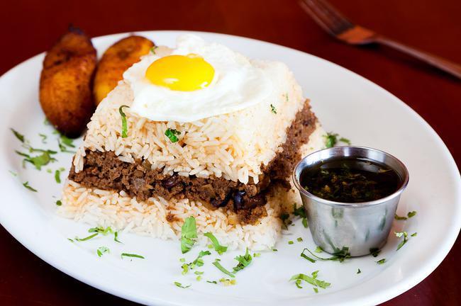 Tapado a lo Pobre · A traditional Peruvian comfort food, ground Certified Angus Beef stew made with raisins, olives, onions, tomatoes and soy sauce, served with garlic jasmine rice, topped with a fried egg and fried sweet plantains.