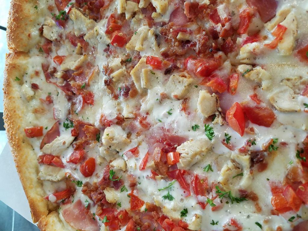 Chicken Bacon Ranch Pizza · Garlic chicken, bacon crumbles, Canadian bacon, and cooked tomatoes, atop a ranch base with a drizzle of ranch on top.