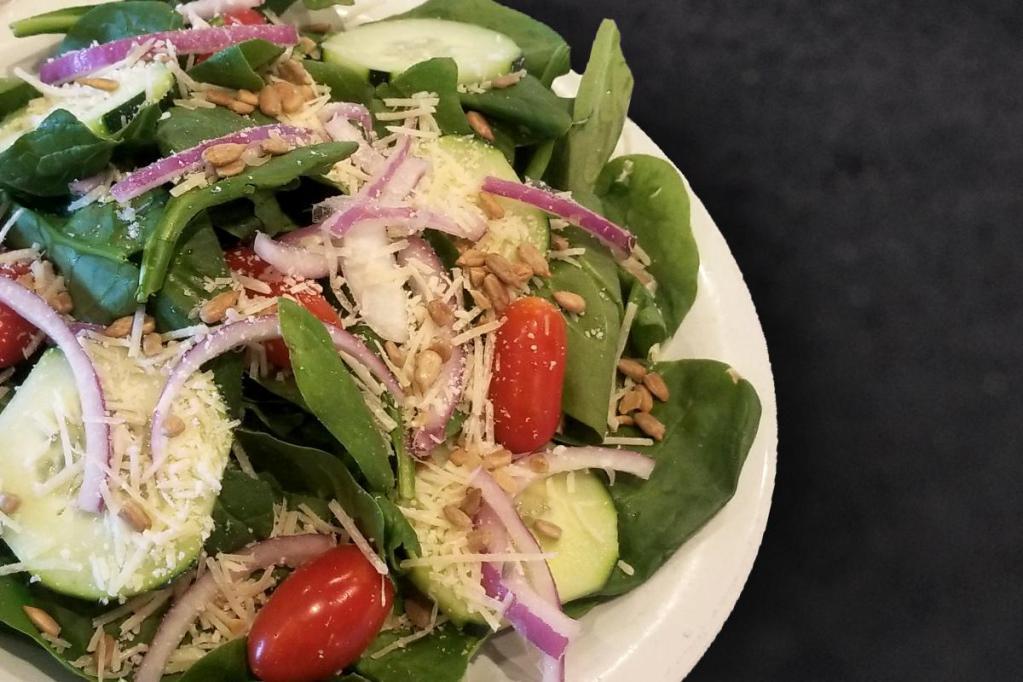 Spinach Salad · Our NEW Spinach salad topped with cucumber, grape tomatoes, red onion, shredded parmesan, sunflower seeds, and balsamic dressing.