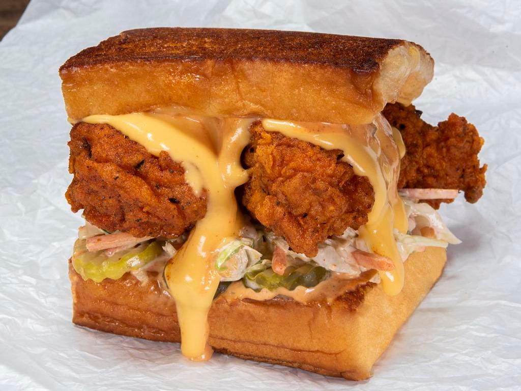The Cheesy Chick · Two crispy fried chicken tenders, spiced to your liking, Plain, Nashville Hot or Nashville Hotter with dill pickle slices, slaw, white American cheese, cheese sauce and chipotle Aioli; served on Kings Hawaiian rolls