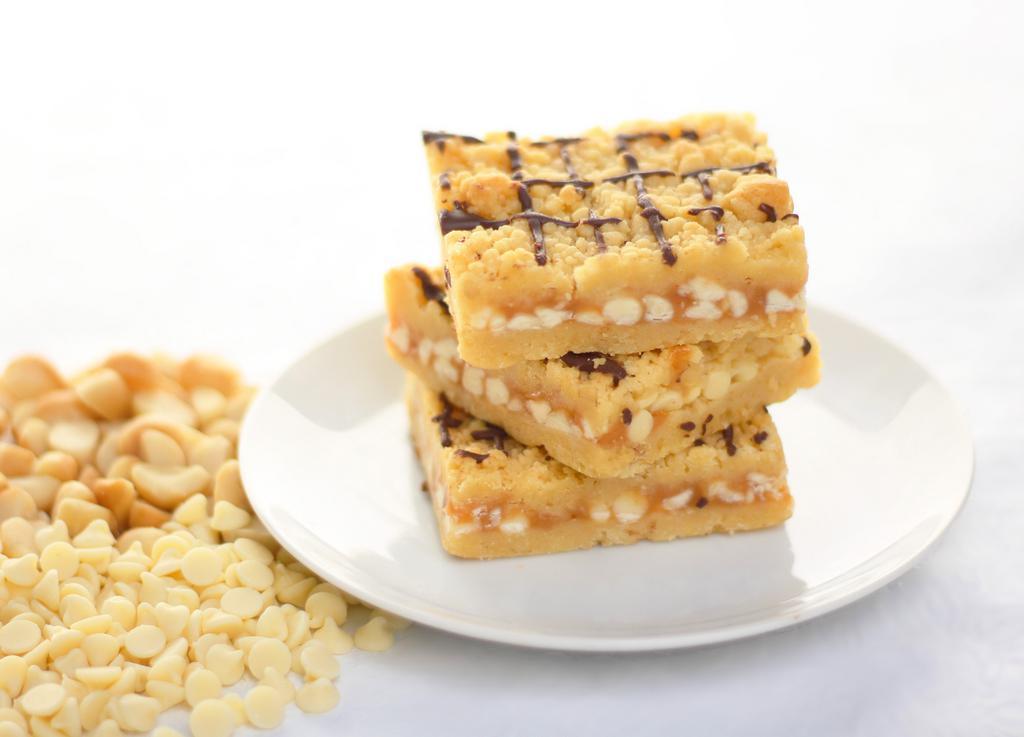 White Chocolate Macadamia Nut Bar · Macadamia nut shortbread surrounds caramel and white chocolate.  Finished with a dark chocolate drizzle. Box of 12 bars. Baked in a facility that uses dairy, nuts, and wheat products.