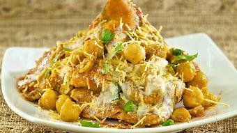 Samosa Chat · Smashed samosa in chickpeas gravy topped with onions yogurt and chutney.