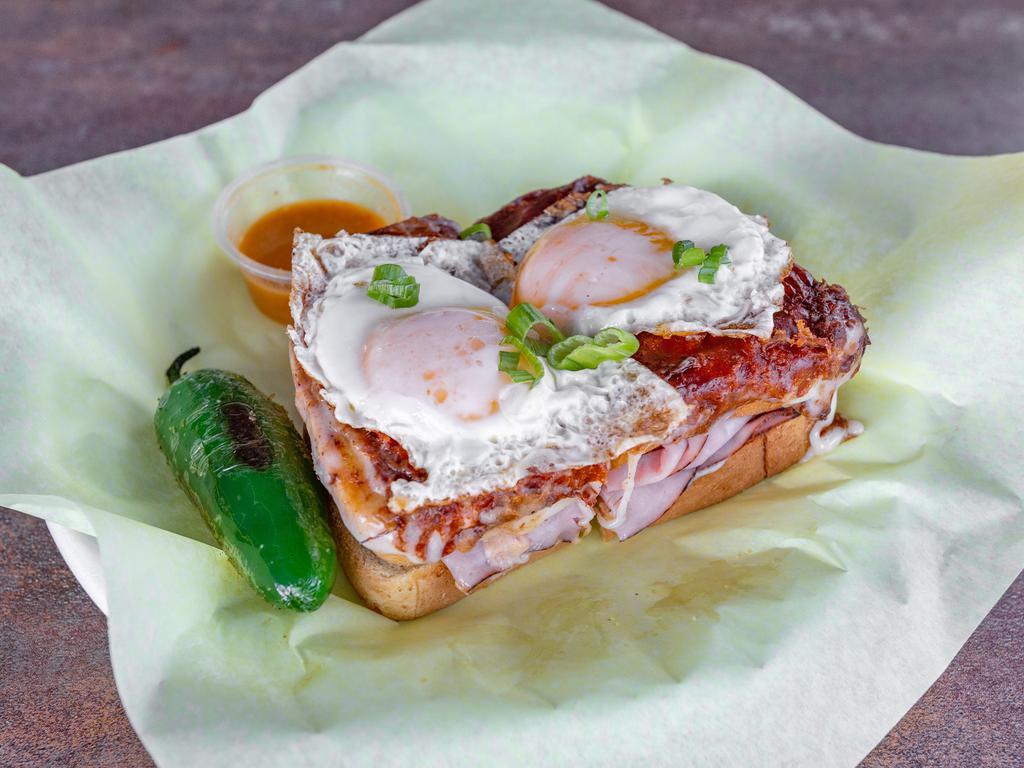 Croque Madame · A classic French sandwich made with fresh sliced ham, layered with bechamel sauce (milk thickened with butter, flour, and cheese), gruyere baked on our boxed French bread, and a sunny side egg on top.