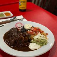 Mole Rojo Con Pollo Plate · Juicy chicken thighs drenched in a rich mole rojo served with rice and beans topped with que...