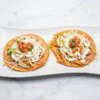 Tostadas Con Tinga  · Two flat corn tortilla shell topped with beans, tinga (shredded chichen in tomato sauce), le...