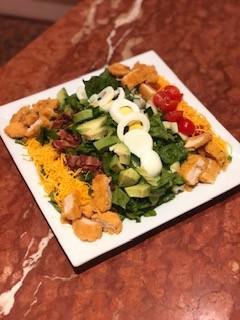 Crispy Chicken Cobb Salad · Fresh romaine lettuce, avocado, bacon, boiled egg, cherry tomatoes, cucumbers and cheddar cheese topped with crispy chicken and served with ranch dressing. 