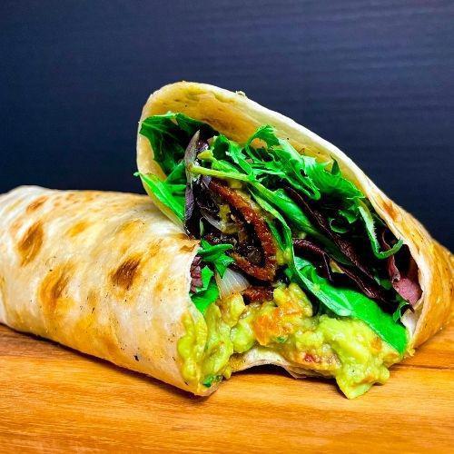 Guac Bacon Wrap · Homemade guacamole, hickory smoked tempeh bacon, tomatoes, grilled onions, mixed greens on a toasted wrap.