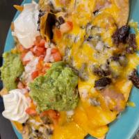 Carne Asada Nachos · Nachos topped with beans, guacamole, sour cream, tomatoes, onions, and cheddar cheese, with ...