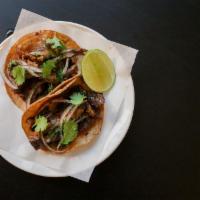 Tacos de Asada · Corn tortilla, flank steak, poblano peppers, roasted onions, red guajillo salsa.