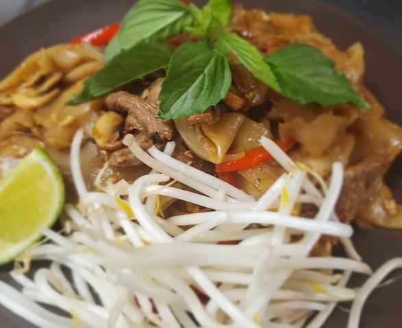 Pad Kee Mao · Wide rice noodles stir-fried with egg, onions, bell peppers, fresh chili, garlic, and basil leaves top with bean sprout, and lime.