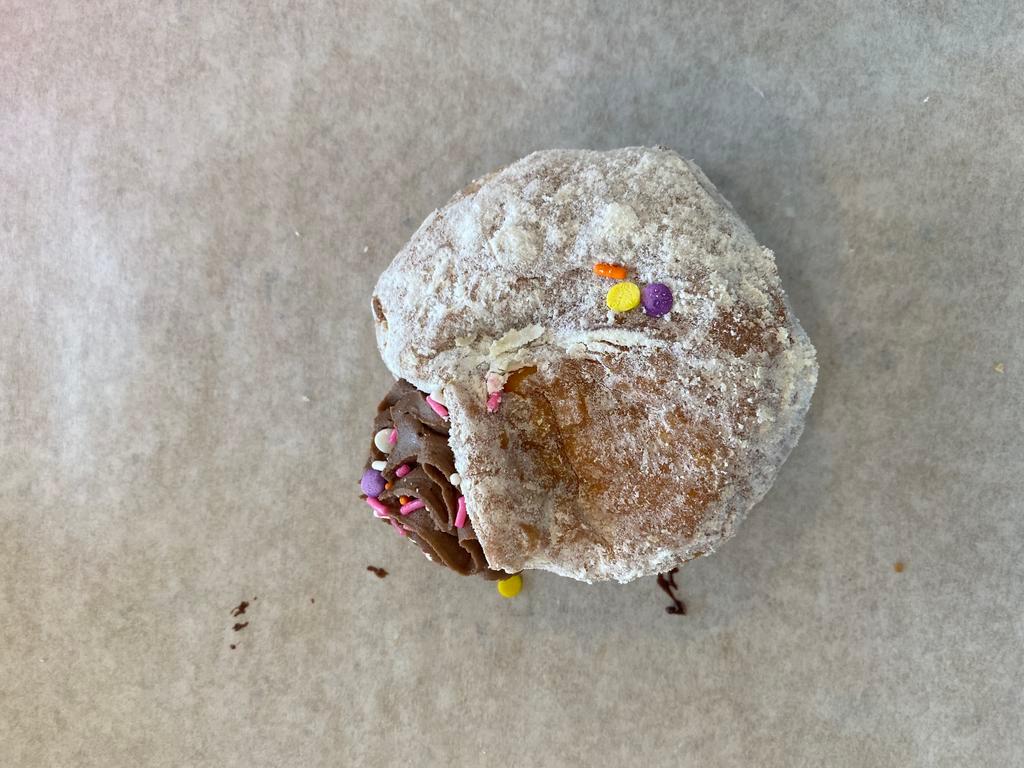 Chocolate Cream Donut · Raised donut coated in powdered sugar, filled with chocolate cream, and topped with sprinkles