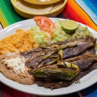 Costillas de Res a La Plancha · Grilled beef ribs. Served with rice, refried beans, salad and guacamole.