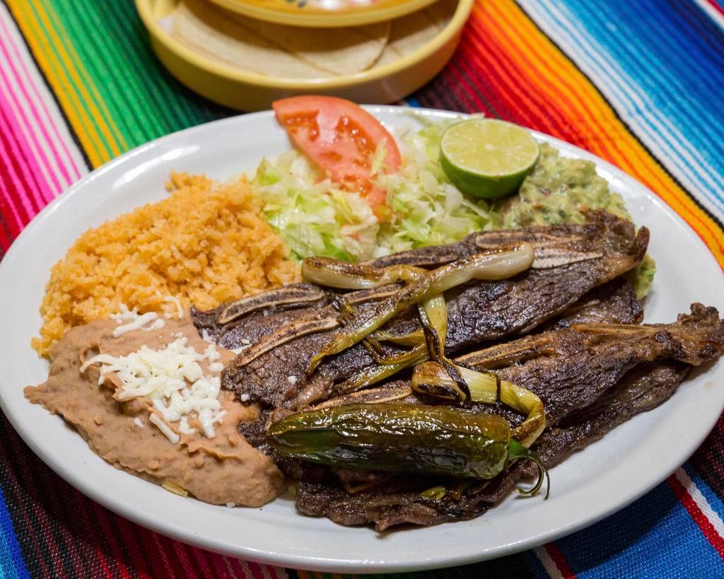 Costillas de Res a La Plancha · Grilled beef ribs. Served with rice, refried beans, salad and guacamole.