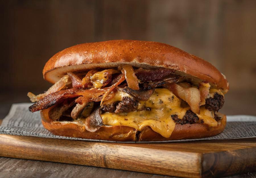 The Hustler Burger · Pretzel bun, double 4 oz. black Angus meat, American cheese, grilled onions, grilled mushrooms, smoked bacon, garlic chipotle sauce and cilantro sauce.