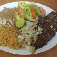 Carne Asada · Grilled seasoned skirt steak topped with sauteed onions. Served with rice and beans and corn...