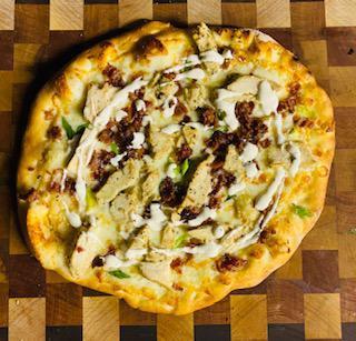 Cowgirl Pizza · Garlic sauce, local cheese, seasoned chicken, bacon, green onion, extra virgin olive oil, herb blend - served with Woodstock buttermilk ranch.