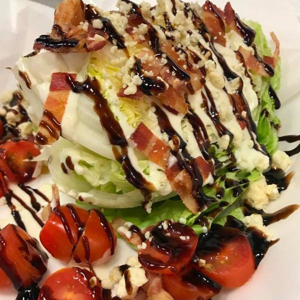 Wedge Salad · Iceberg wedge topped with bleu cheese crumbles, grape tomatoes, bacon, balsamic reduction, and bleu cheese dressing.