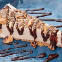 Butterfinger’d Cheesecake · New York baked cheesecake topped with delicious chocolate sauce and butter finger crumbles.