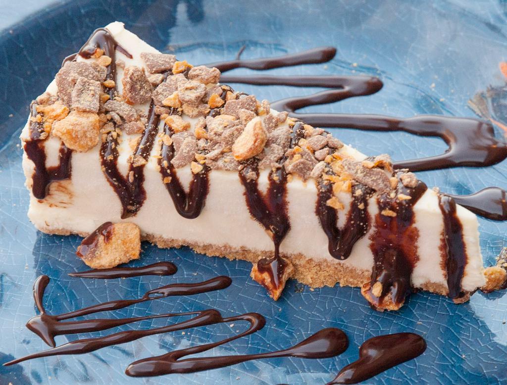 Butterfinger’d Cheesecake · New York baked cheesecake topped with delicious chocolate sauce and butter finger crumbles.