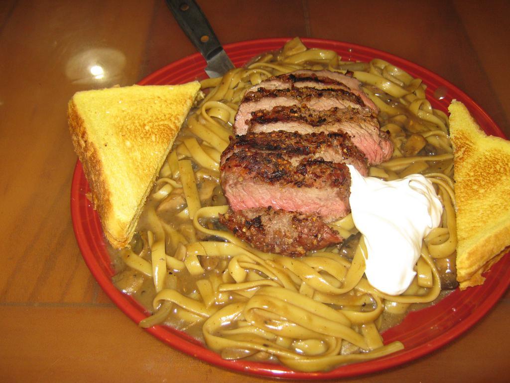 Beef Stroganoff · An 8 oz. iron steak cooked to order on top of a pile of fettuccini noodles with sauteed mushrooms and onions with a creamy beef sauce topped with a dab of sour cream and garlic toast.
